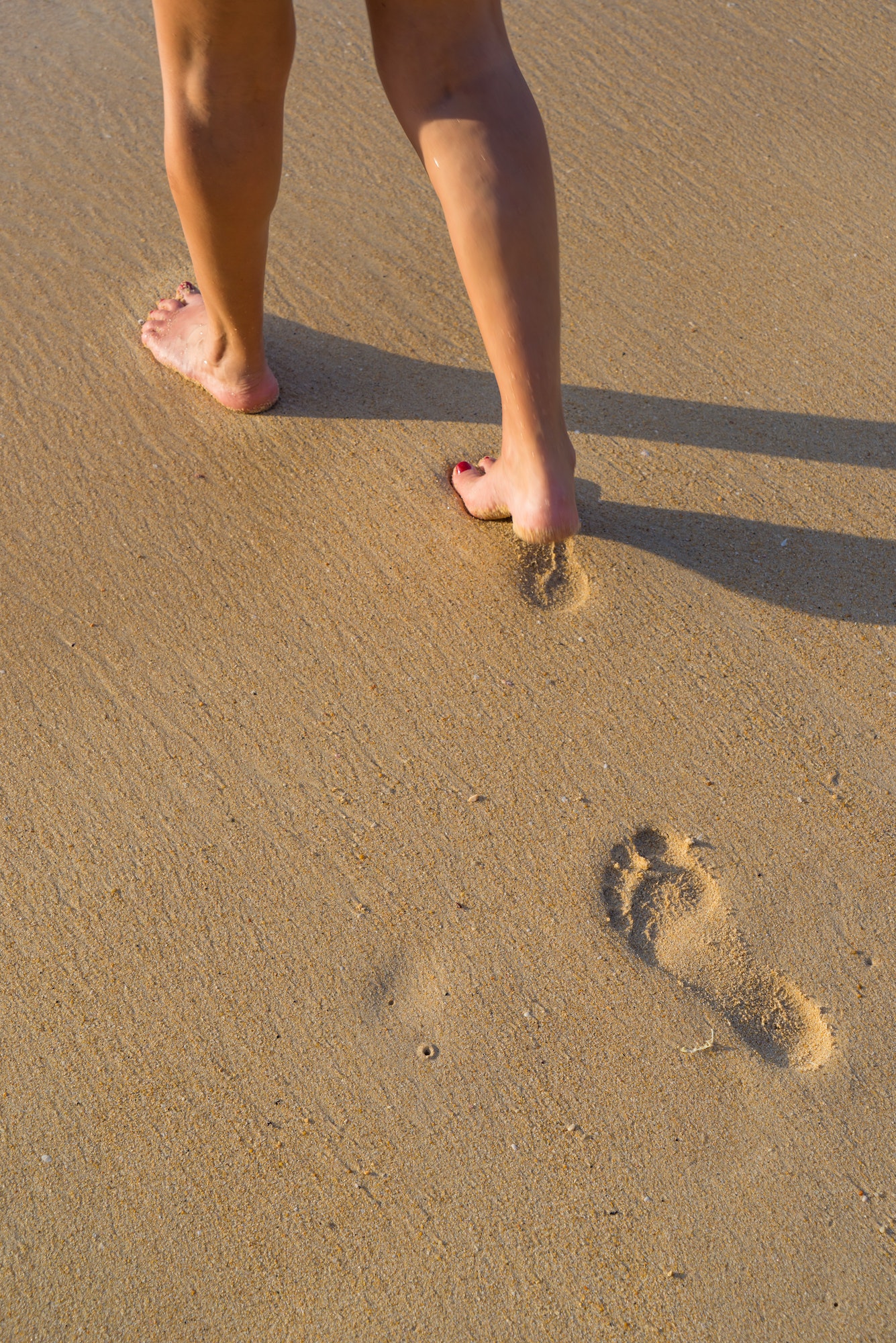 woman walking on sand beach leaving footprints in the sand.